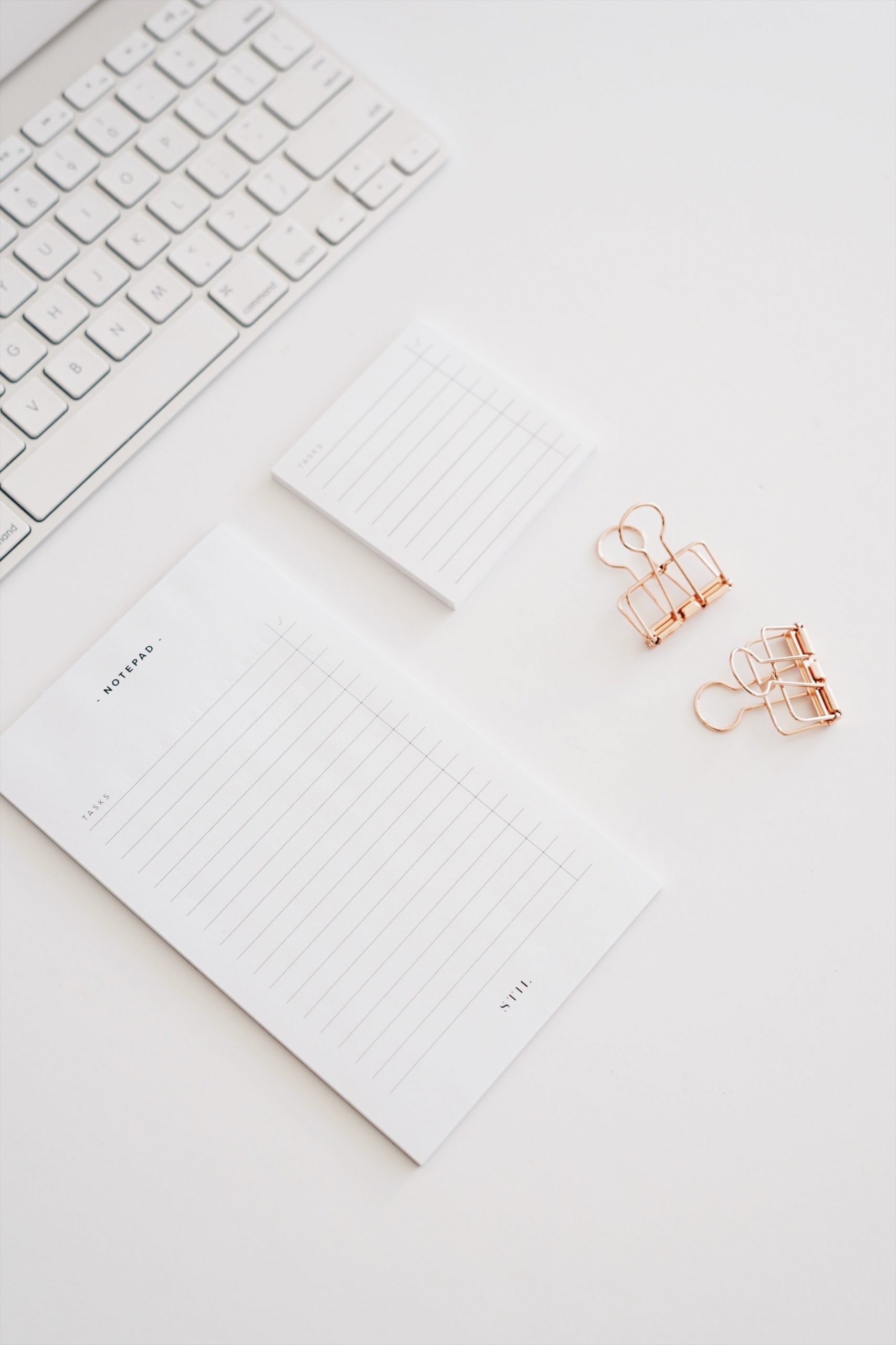 White keyboard, notebooks and copper bulldog clips