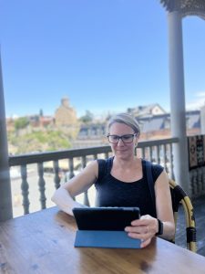 Woman working on a tablet, with a bright blue sky and blurred buildings in the background