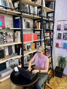Woman working on a laptop at a cafe with a wall of books on her right